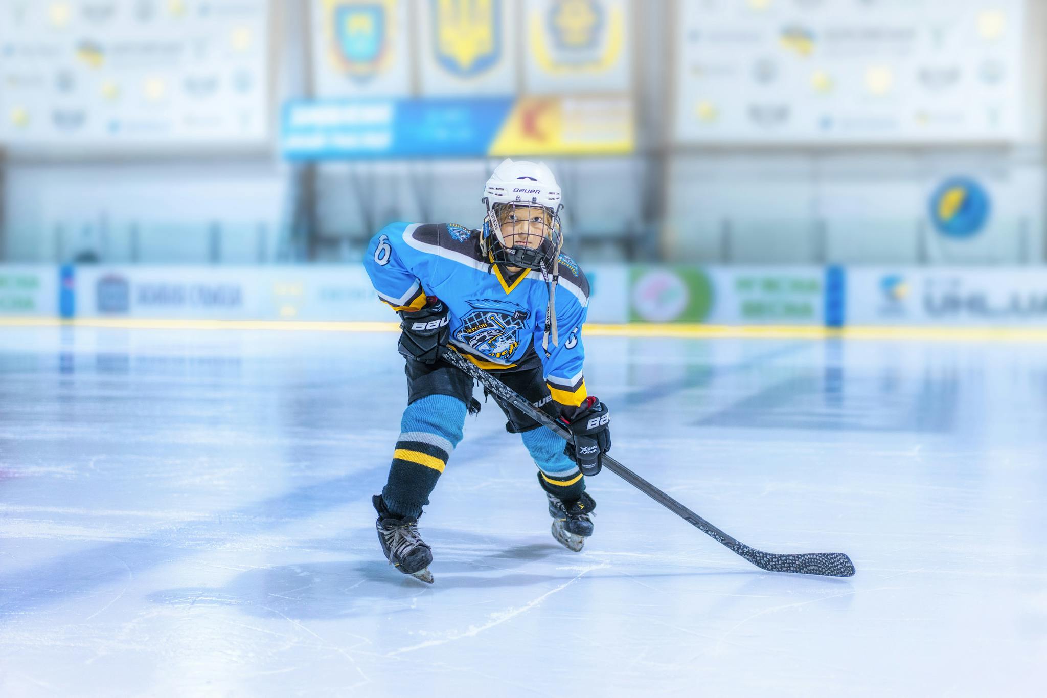 A young hockey player in full gear practicing on an ice rink indoors.