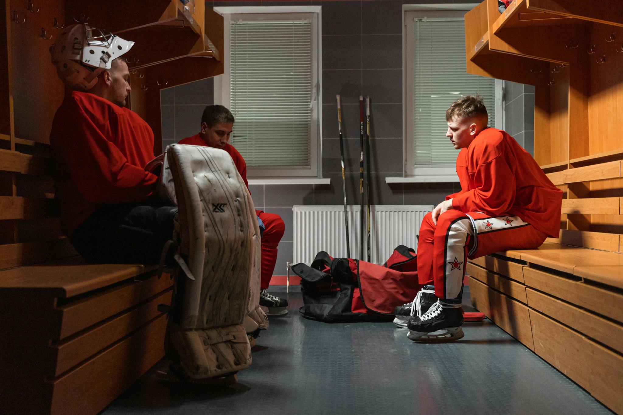 Three ice hockey players in a locker room wearing uniforms, getting ready for a game.